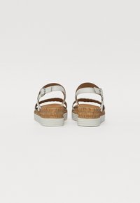 Brown and white sandals with a woven cork-like design, adjustable ankle straps, and a flat white sole. Textured footbed visible.
