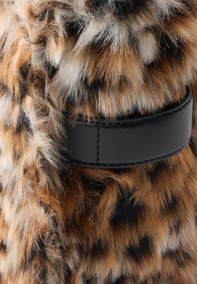 Gros plan de fausse fourrure marron et noire tachetée avec une sangle en cuir noir cousue au centre.