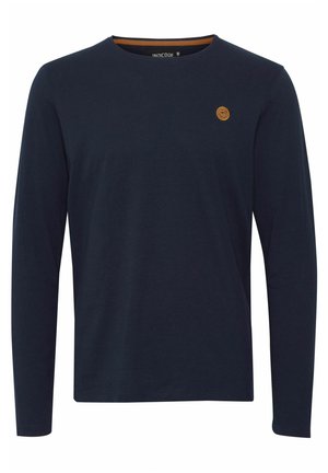 Marineblaues Langarmshirt aus Baumwolle, mit Rundhalsausschnitt, kontrastierender innere Kragenverzierung und einem kleinen braunen Logopatch auf der Brust.