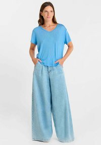 Luchtblauw T-shirt met korte mouwen, gecombineerd met lichtblauwe, wijd uitlopende denimbroek. Het T-shirt heeft een ronde hals en een ontspannen pasvorm.