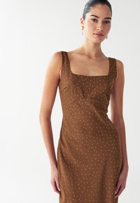 Vestido marrón sin mangas con escote cuadrado, con lunares blancos, cuerpo ajustado y una textura suave.