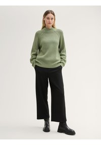 Groene geribbelde gebreide trui met hoge hals, gecombineerd met zwarte brede broek en zwarte enkellaarsjes. Eenvoudig ontwerp met gestructureerde stof.