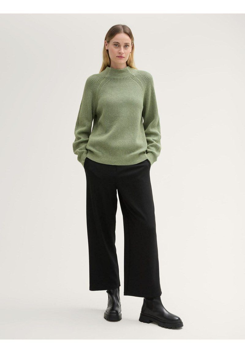 Groene geribbelde gebreide trui met hoge hals, gecombineerd met zwarte brede broek en zwarte enkellaarsjes. Eenvoudig ontwerp met gestructureerde stof.