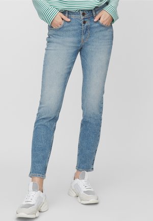 Person wearing light blue slim-fit jeans, green and white striped long sleeve shirt, and white chunky sneakers, hands in front pockets.