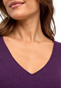 Top viola a costine con scollatura a V profonda, texture liscia e sottile lucentezza. Il tessuto aderisci alla scollatura e alle spalle.