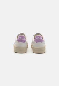 Vita lädersneakers med en beige sula, lila hälflik och kontrasterande vit "VEJA"-logotyp; rund tådesign med minimalistisk stil.