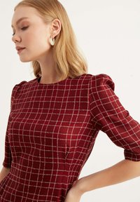 Röd rutig klänning med korta puffärmar, strukturerad tyg, vit rutmönster, rund halsringning och figursydd silhuett.