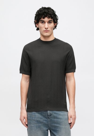 Krátky rukáv tmavosivej košele s textúrovaným cikcak vzorom, okrúhlym výstrihom a rebrovanými manžetami, doplnený svetlomodrými džínsami.