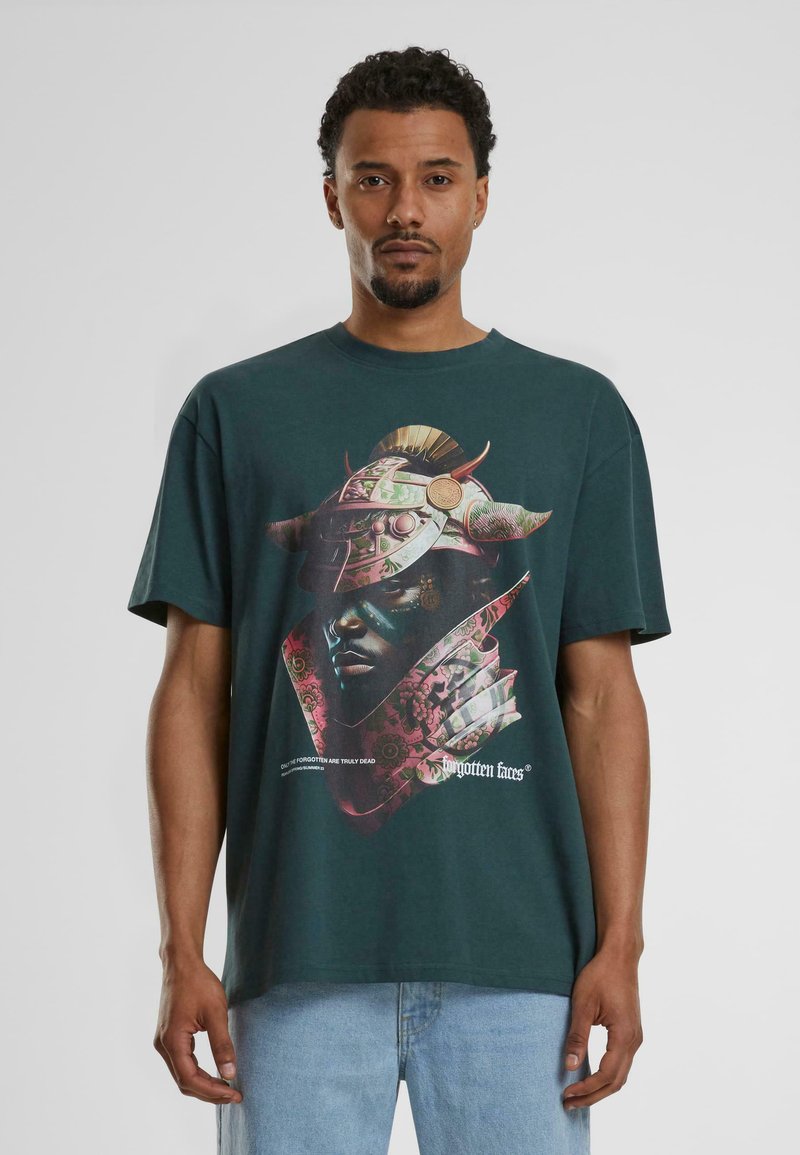 Zielony bawełniany t-shirt z graficznym nadrukiem przedstawiającym zamaskowaną twarz z rogami i elementami kwiatowymi. Luźny krój z krótkimi rękawami.
