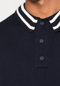 Polo de punto en color marino con un cuello de canalé de rayas blancas, con tres botones en la parte delantera y un acabado texturizado.