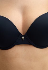 Navy blue padded bra with a smooth texture. Features a decorative silver charm at the center and seamless cups for a streamlined appearance.