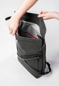Schwarzer wasserdichter Rucksack mit strukturierter Form, vorderer Reißverschlusstasche, roten Akzenten und grauem Futter mit Gittermuster.