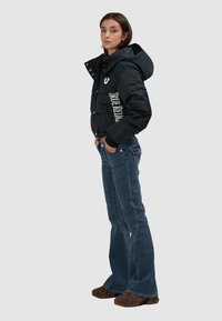 Czarna kurtka puchowa z kapturem, z białym logo z boku, połączona z dżinsami w kolorze ciemnego niebieskiego o rozszerzających się nogawkach oraz butami w panterkę.