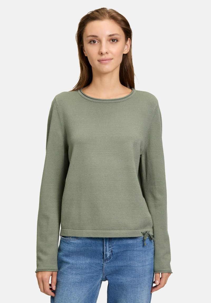 Hellgrüner Langarmpullover mit rundem Halsausschnitt, weichem Material und einer Kordelzugdetail am Saum. Dazu eine blaue Jeans.
