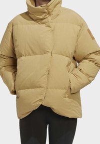 Béžová péřová bunda s vysokým límcem, prošívaným designem a mírně zkráceným střihem, s božní nášivkou a předním zapínáním na knoflíky.