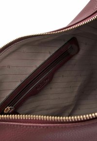 Intérieur d'un sac à main en cuir bordeaux avec fermeture éclair dorée, doublure lisse et une poche zippée intérieure avec une étiquette en cuir assortie.