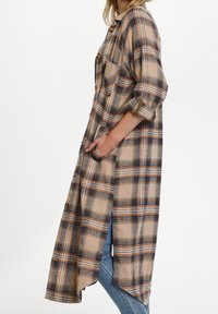 Rutiga klänning i beige, blått och orange, med en lång, ledig modell, knäppning framtill, två framfickor och uppvikta ärmar.