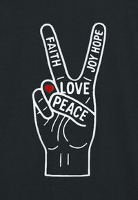 Svart tyg med en vit grafik av en upphöjd hand som formar ett fredstecken, där orden "TRO", "KÄRLEK", "GLÄDJE", "HOPP" och ett rött hjärta visas.