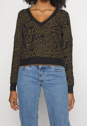 Braun und schwarz gemusterter Pullover mit V-Ausschnitt, gerippten Bündchen und Saum, kombiniert mit hellblauen Jeans. Die Textur scheint gestrickt zu sein.