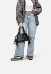 Borsa a tracolla in pelle nera con dettagli in frange, forma strutturata e manici intrecciati. Abbinata a jeans oversize chiari e sneakers verdi.