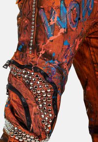 Oranje stoffen broek met een verfspetterontwerp met blauwe en roze accenten. Details omvatten studs, ritsen en gestructureerde secties.