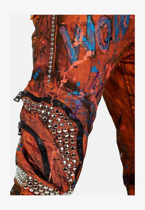 Oranje stoffen broek met een verfspetterontwerp met blauwe en roze accenten. Details omvatten studs, ritsen en gestructureerde secties.