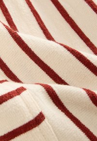 Tissu rayé avec de larges rayures rouges sur fond crème, présentant une surface texturée et douce adaptée aux vêtements ou à la décoration intérieure.