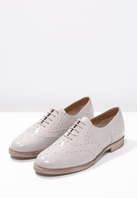 Chaussures brogues gris clair en cuir verni, dotées de perforations décoratives, d'un petit talon en bois et d'un design classique à lacets.