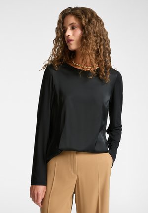 Maglietta nera a maniche lunghe realizzata in tessuto morbido con scollatura rotonda. Abbinata a pantaloni beige chiaro. Leggero lucido e vestibilità rilassata.