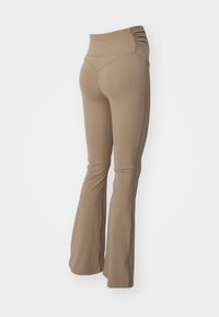 Växande yogabyxor i beige tyg, med en hög, samlad midja och slät textur, designade för komfort och flexibilitet under rörelse.