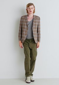 Plaid blazer in brown and beige over a gray t-shirt, paired with olive cargo pants and white sneakers with brown soles.