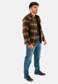 Brązowa i beżowa koszula w kratę flanelową, czarna koszulka pod spodem, jasnoniebieskie dżinsy i czarne trampki z miętowymi akcentami.