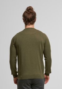 Suéter de color verde oliva hecho de una tela suave, con mangas largas y escote redondo. El diseño incluye puños y dobladillo acanalados.