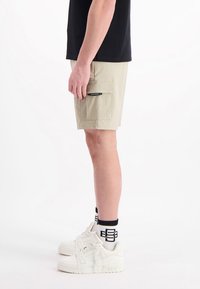 Beige cargoshorts met zijzakken, gedragen met een zwart T-shirt en witte sneakers. Witte en zwarte gestreepte sokken zichtbaar.