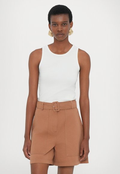 Un débardeur blanc côtelé associé à un short marron taille haute avec une large ceinture et des plis marqués sur le devant.