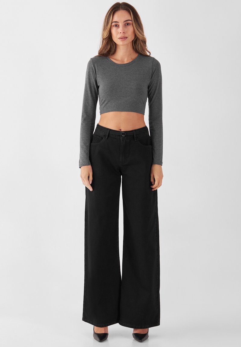 Grauer langärmeliger, kurz geschnittener Pullover, kombiniert mit hoch taillierten schwarzen Weitbeinhosen. Glattes Material und maßgeschneiderter Schnitt mit Knopfverschluss.
