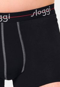 Schwarze Baumwoll-Boxershorts mit grauen Nähdetails und einem Bund, der den Markennamen "sloggi" in grauer und roter Schrift zeigt.