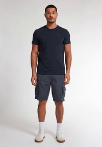 Donkerblauw T-shirt met korte mouwen, gecombineerd met grijze cargoshorts met zijzakken. Witte sokken en witte sneakers maken de outfit compleet.