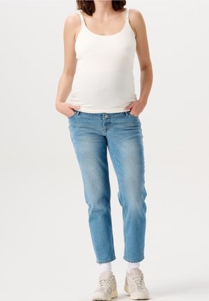 Valkoinen hihaton toppi säädettävillä olkaimilla yhdistettynä vaaleansinisiin korkeavyötäröisiin farkkuihin ja beigeihin tennareihin. Yksinkertainen, rento muotoilu.