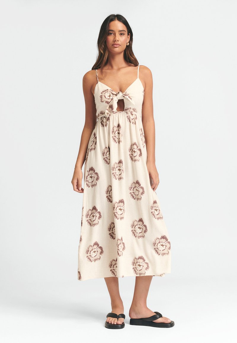 Maxi šaty z krémové látky s hnědými květinovými vzory, které mají nastavitelné ramínka, detail uzlu na přední straně a výřez v tvaru klíče.