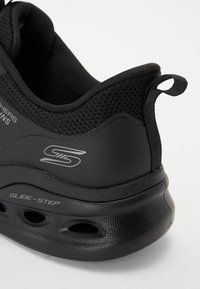 Mustmust mustreitud spordijalats, millel on võrgusilma ülemine osa, ümar konts, tekstuuriga kummitald ja küljes hõbedane "GLIDE-STEP" bränding.