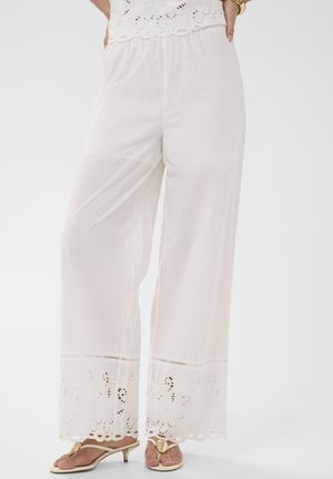 Pantalon blanc à jambes larges avec bordure en dentelle ajourée à l'ourlet, porté avec un top assorti en dentelle et des sandales à talons beiges.