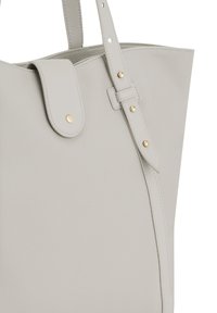 Sac fourre-tout en simili cuir gris clair avec une large ouverture, un rabat supérieur et des sangles latérales ajustables. Doté d'accents en métal doré.