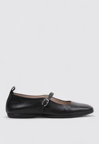Zapato plano de cuero negro con punta puntiaguda y correa ajustable con hebilla, suela sencilla y tirador en el talón.