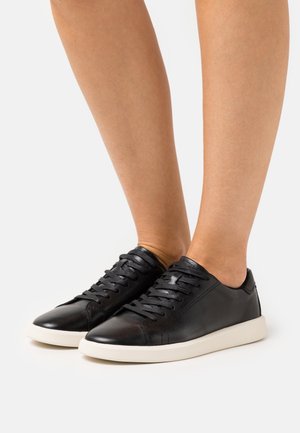 Black leather sneakers with a smooth finish, round toe, and 6 eyelet lace-up design. Features white rubber sole and minimalistic stitching.