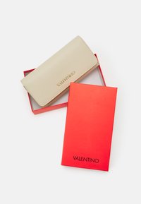 Beige leather wallet with textured surface, featuring gold "VALENTINO" logo. Presented in a red box with a black logo.