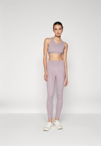 Lys lavendel sports-bh og høyt midjebånd leggings laget av elastisk stoff, kombinert med hvite treningssko. Sømløst design og tettsittende snitt.