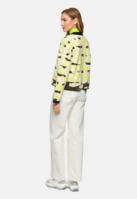 Übergroße Jacke mit einem Tarnmuster in Grün und Beige, kombiniert mit weißen weiten Hosen und grauen Sneakers.