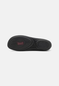 Suela de zapato de goma negra con diseño curvado, que presenta una marca destacada y acentos texturizados. Incluye un patrón de banda de rodadura circular para mayor agarre.