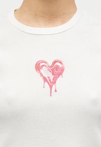 Λευκό βαμβακερό t-shirt με γυαλιστερό ροζ καρδιά γραφικό και λεπτομέρειες τήξης που στάζουν. Στρογγυλή λαιμόκοψη με ομαλή υφή.